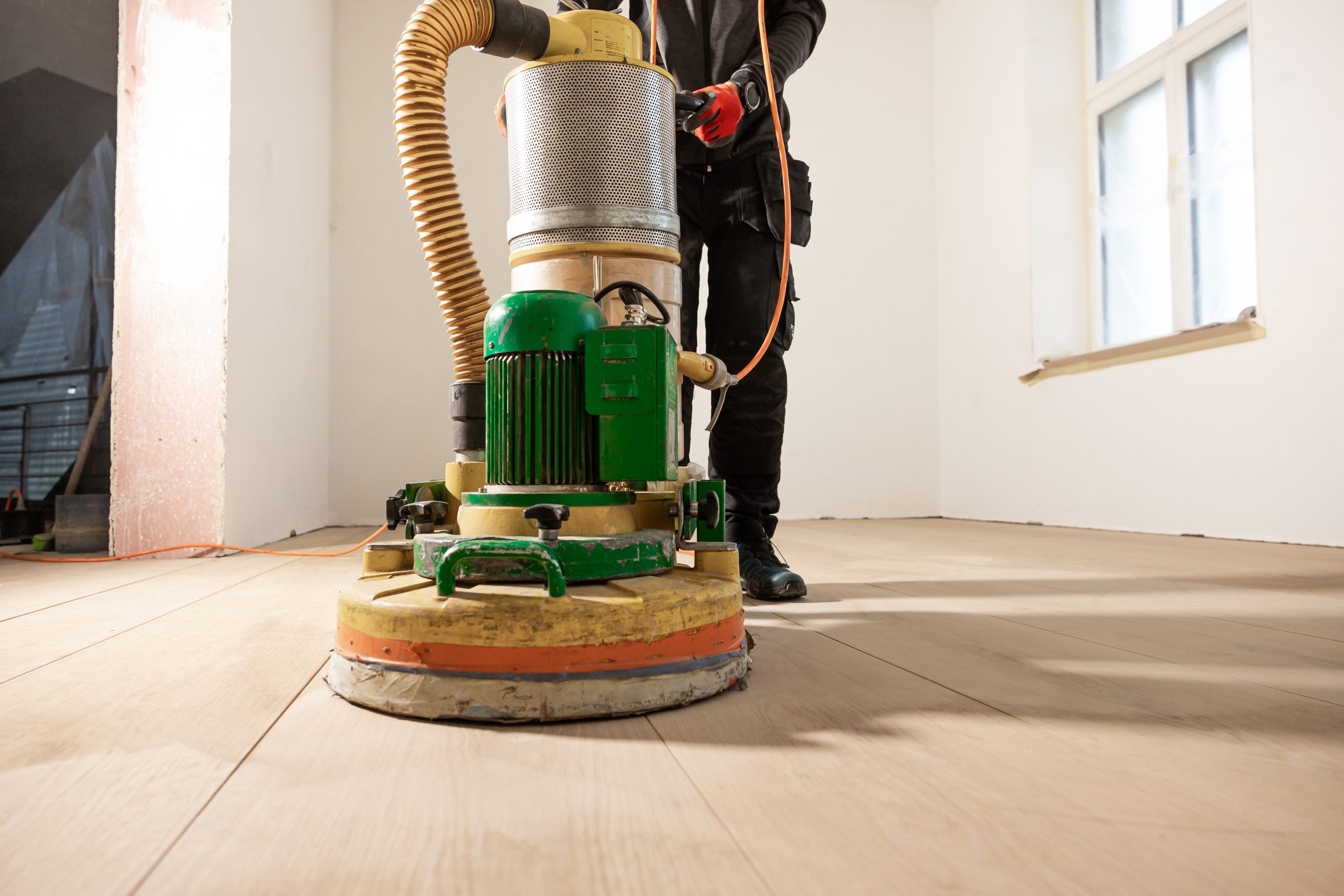 Worker Polishing Wooden Floor in Bright Unfurnished Room